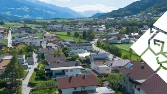 Luftaufnahme einer Wohnsiedlung mit grünen Feldern und majestätischem Bergblick im Hintergrund.