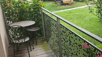 Gemütlicher Balkon mit Holzboden und Blick auf den grünen Gemeinschaftsgarten, ideal für entspannte Stunden im Freien.