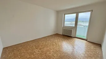 Heller, leerer Wohnraum mit Parkettboden und Zugang zu einem kleinen Balkon.