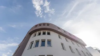 Moderne Gebäudefassade mit geschwungenen Linien und zahlreichen Fenstern unter blauem Himmel.