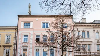 Historisches Gebäude mit rosa Fassade und dekorativen Elementen an einer belebten Straße.