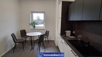 Kompakte Küchenzeile mit dunklen Oberschränken und einem kleinen Essbereich am Fenster.