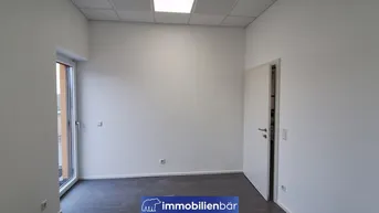 Heller, leerer Büroraum mit dunklem Laminatboden und Zugang zu einem sonnigen Außenbereich.