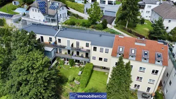 Luftaufnahme eines Wohnkomplexes mit mehreren Gebäuden, umgeben von viel Grün und Bäumen.