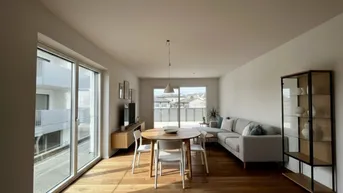 Helles Wohn- und Esszimmer mit Holzboden, großen Fenstern und Zugang zu einem Balkon.