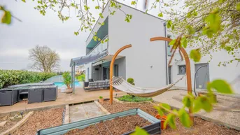 Seitlicher Gartenbereich mit Hochbeeten, Hängematte und Blick auf die moderne Hausfassade.