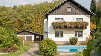 Charmantes Einfamilienhaus mit Balkon, Garten, Pool und separater Garage, umgeben von viel Grün.