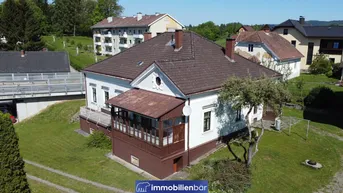 Historisches Wohnhaus mit braunem Dach und Veranda, umgeben von einer grünen Wiese.