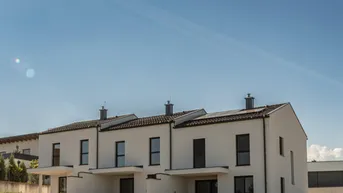 Reihe moderner Reihenhäuser mit weißer Fassade, dunklen Dächern und Photovoltaikanlagen.