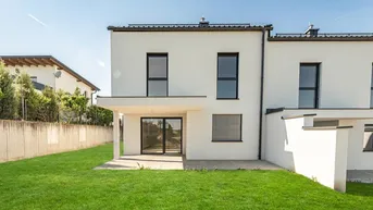 Moderne Reihenhausfassade mit weißem Putz, großen Fenstern und einer grünen Rasenfläche.