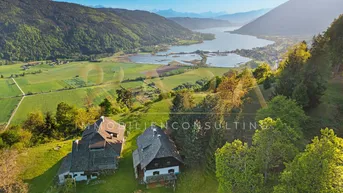 Luftaufnahme der Liegenschaft mit zwei Häusern, umgeben von grünen Hügeln und einem See im Hintergrund.