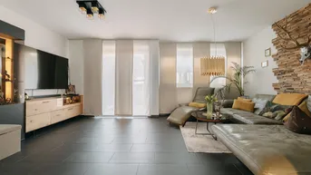 Geräumiges Wohnzimmer mit dunklen Fliesen, bequemer Couch und dekorativer Holzwand.