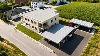 Luftaufnahme eines modernen Wohngebäudes mit Flachdach und Carports neben einem grünen Feld.
