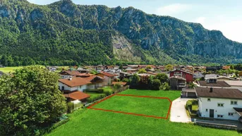 Grünes Baugrundstück mit Bergblick, umgeben von Wohnbebauung in ländlicher Umgebung.