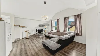 Geräumiger Wohn- und Essbereich mit gemütlichem Sofa, Holzboden und schrägen Decken im Dachgeschoss.