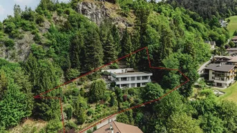 Luftaufnahme eines Hauses am Hang mit viel Grün und umrandetem Grundstück.