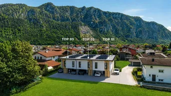 Moderne Reihenhäuser mit Photovoltaikanlage und Carports vor einer beeindruckenden Bergkulisse.