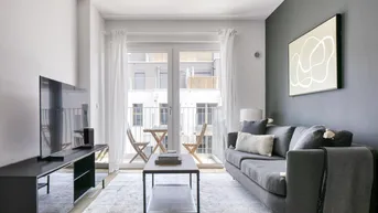 Modernes Wohnzimmer mit grauem Sofa, Fernseher und Zugang zu einem kleinen Balkon.
