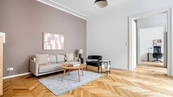 Helles Wohnzimmer mit Fischgrätparkett, moderner Einrichtung und Zugang zu einem weiteren Raum.