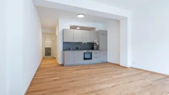 Heller Wohnbereich mit Holzboden und integrierter Küchenzeile in modernem Design.