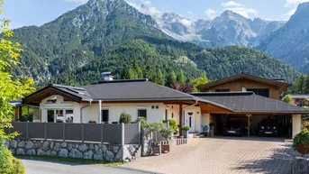 Einfamilienhaus mit gepflasterter Auffahrt und Carport vor beeindruckender Bergkulisse.