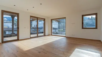 Heller Wohnbereich mit Holzboden, großen Fenstern und Zugang zu einem Balkon mit Bergblick.