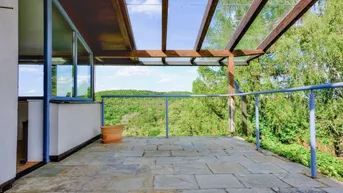 Geräumige Terrasse mit Steinfliesen und weitem Blick über die grüne Landschaft.