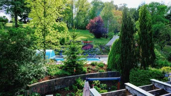 Weitläufiger Gartenbereich mit Swimmingpool, umgeben von üppiger Vegetation und Bäumen.