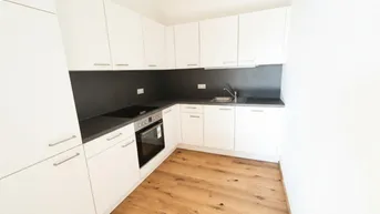 Moderne Einbauküche mit weißen Schränken, dunkler Arbeitsplatte und Holzfußboden.