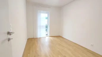 Helles Zimmer mit Parkettboden, weißen Wänden und Zugang zu einem Balkon oder einer Terrasse.