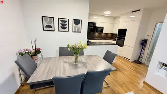 Moderner offener Essbereich mit Holzboden und Blick auf die integrierte Küche mit weißen Hochglanzfronten.
