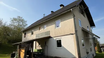 Seitenansicht eines ländlichen Hauses mit Satteldach und einfacher Fassade unter blauem Himmel.