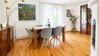 Helles Esszimmer mit Holzboden, großem Esstisch und einem traditionellen Kachelofen.