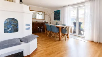 Heller Wohn- und Essbereich mit traditionellem Kachelofen, Holzboden und Zugang zum Balkon.