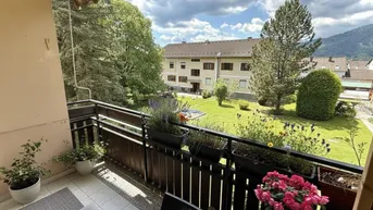 Gemütlicher Balkon mit Pflanzen, Sitzgelegenheiten und Blick auf den grünen Innenhof und die Berge.