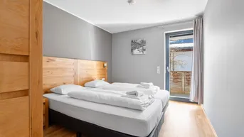 Helles Schlafzimmer mit zwei Einzelbetten, Holzbettrahmen und Zugang zum Balkon.