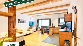 Offener Wohnbereich mit Holzbalkendecke, integrierter Küche und Schlafgelegenheit, ideal als Freizeitwohnsitz.