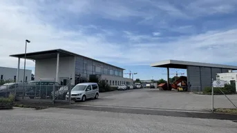 Ansicht des modernen Bürogebäudes mit großem Parkplatz und umliegendem Industriegelände unter bewölktem Himmel.