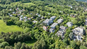 Weitläufige Luftaufnahme der grünen Umgebung mit vielen Häusern und bewaldeten Hügeln im Hintergrund.