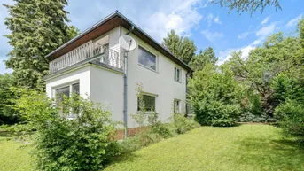 Weißes Einfamilienhaus mit Balkon und großem Garten umgeben von viel Grün.