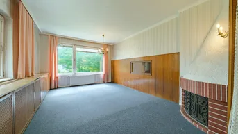Helles Wohnzimmer mit Kamin, großen Fenstern und Teppichboden, bereit zur Renovierung.