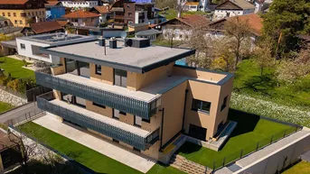 Moderne Wohnanlage mit mehreren Balkonen und Flachdach, umgeben von gepflegtem Rasen und weiteren Häusern.