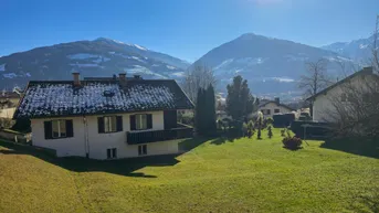 Haus mit Garten und Bergblick unter strahlend blauem Himmel und sonnigem Wetter.