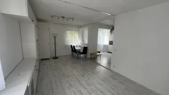 Heller Wohn- und Essbereich mit weißer Schrankwand, Esstisch und Blick in den angrenzenden Küchenbereich.