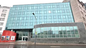 Modernes Bürogebäude mit großer Glasfassade und grauen Steinelementen an einem bewölkten Tag.