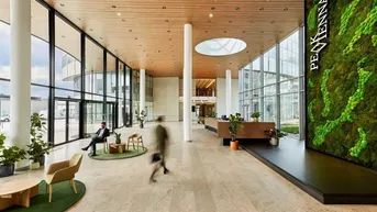 Großzügige, moderne Lobby mit hohen Decken, viel Tageslicht und einer Mooswand als Blickfang.