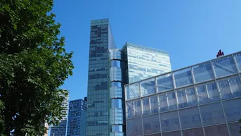 Moderne Hochhäuser mit Glasfassaden unter blauem Himmel, umgeben von Bäumen und städtischer Architektur.