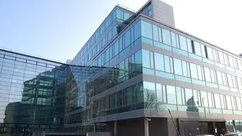 Modernes Bürogebäude mit auffälliger Glasfassade und reflektierenden Fenstern unter klarem Himmel.
