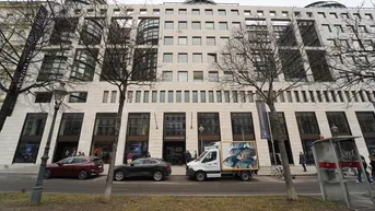 Moderne Geschäftsfassade eines großen Gebäudes mit vielen Fenstern und Geschäften im Erdgeschoss.