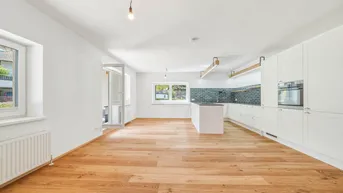Heller offener Wohn- und Essbereich mit moderner Einbauküche, Holzboden und Zugang zum Außenbereich.
